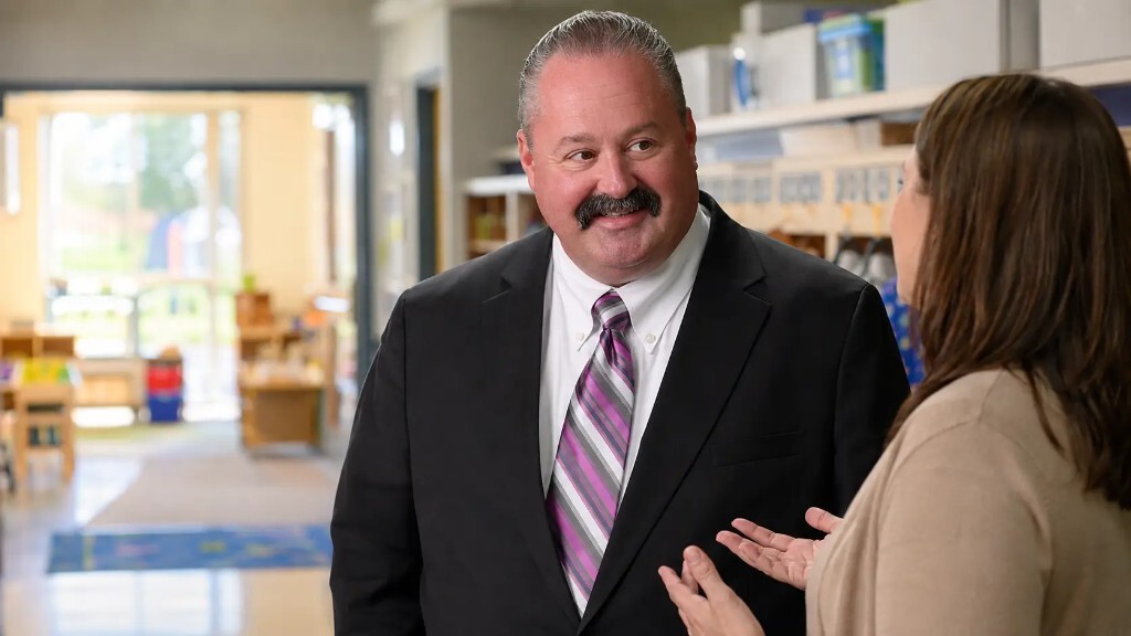Greg in a classroom, mid-conversation with a director