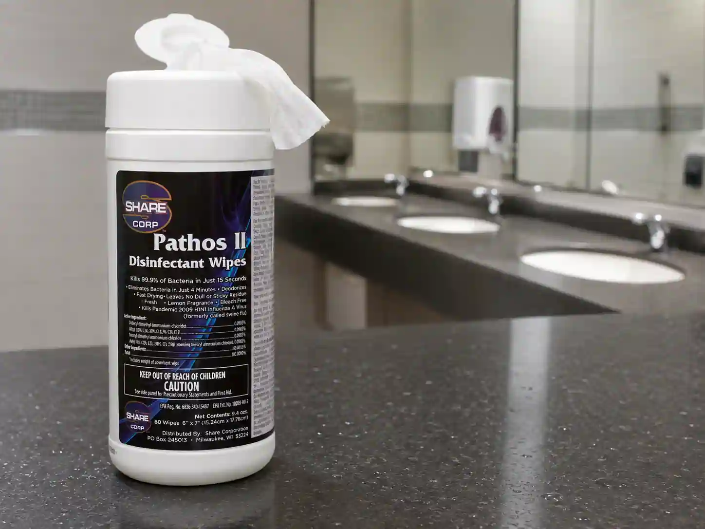 PATHOS II disinfectant wipe canister on a school desk with a wipe pulled from the lid, classroom seating in the background